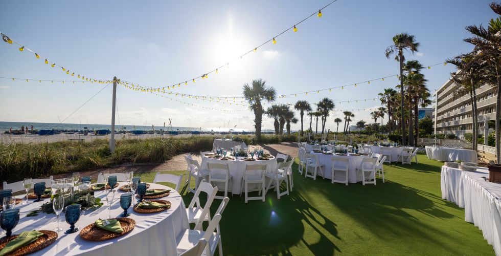 A Set Of Tables Set Up On A Lawn With A Body Of Water In The Background
