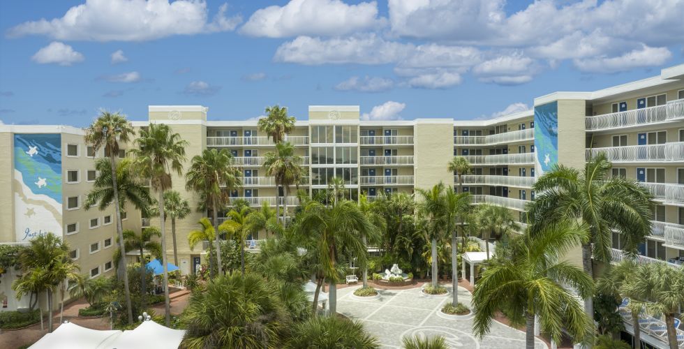 A Building With Palm Trees And A Body Of Water In The Background